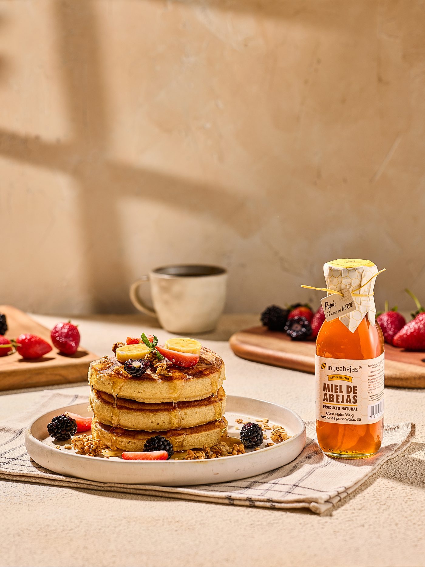 Pancakes con frutos rojos y granola junto a un frasco de miel Ingeabejas, luz cálida de mañana