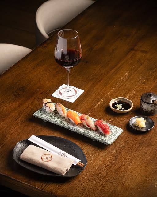 Tabla de sushi con copa de vino sobre madera oscura