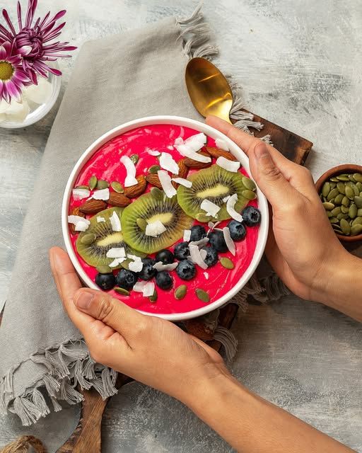 Bowl de frutas y granola sostenido por dos manos sobre mantel de lino